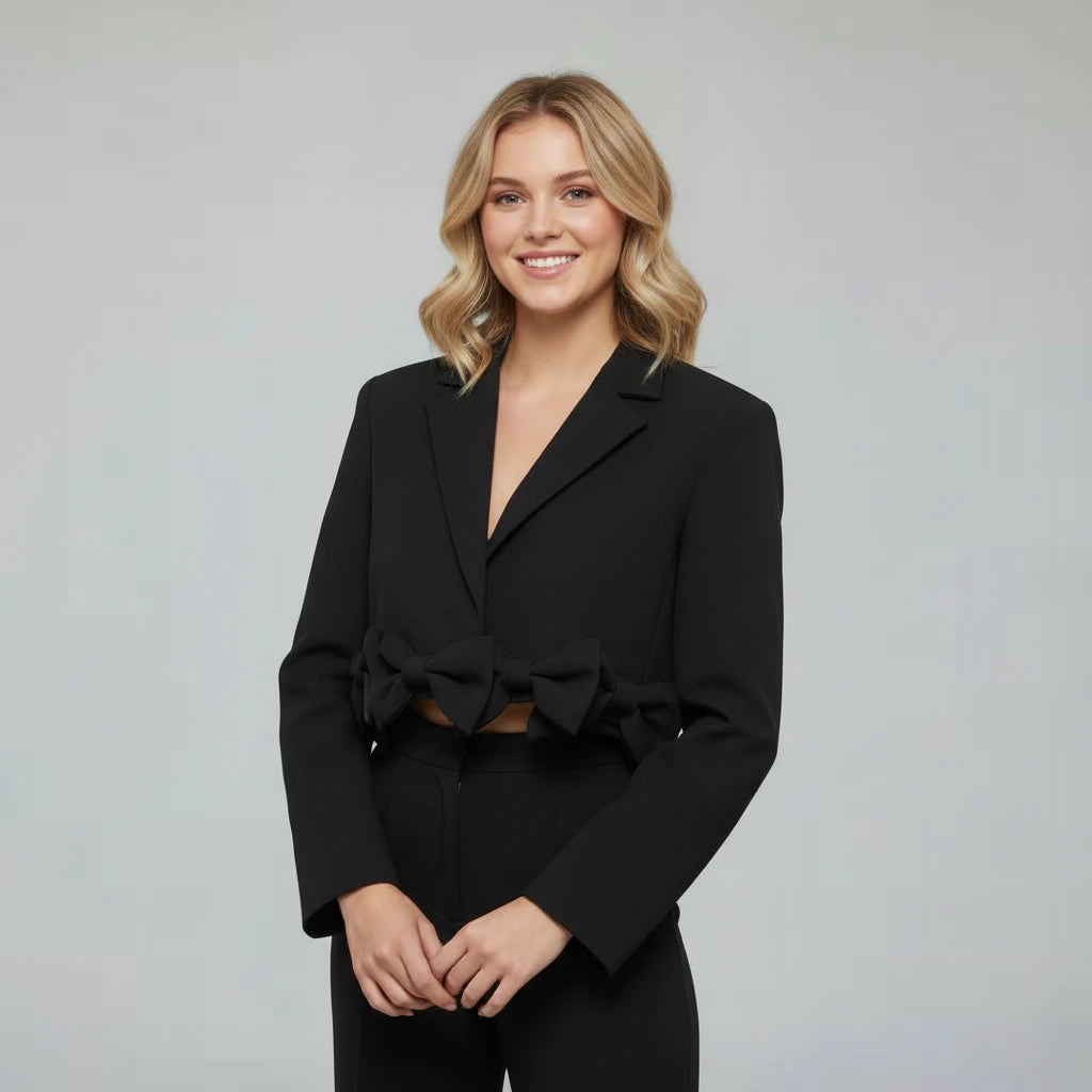 Woman wearing a black blazer with bow details on a gray background