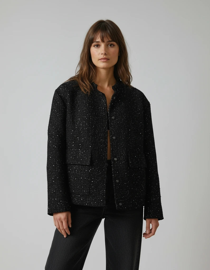 Woman wearing a black speckled jacket against a plain background