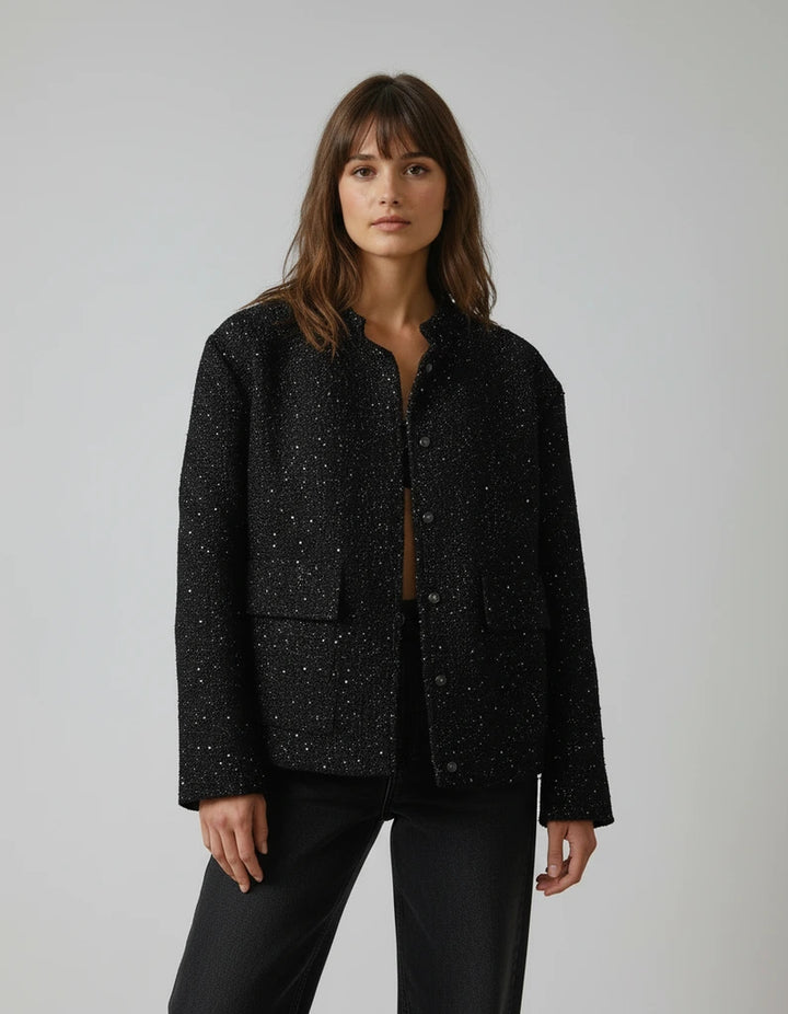 Woman wearing a black speckled jacket against a plain background