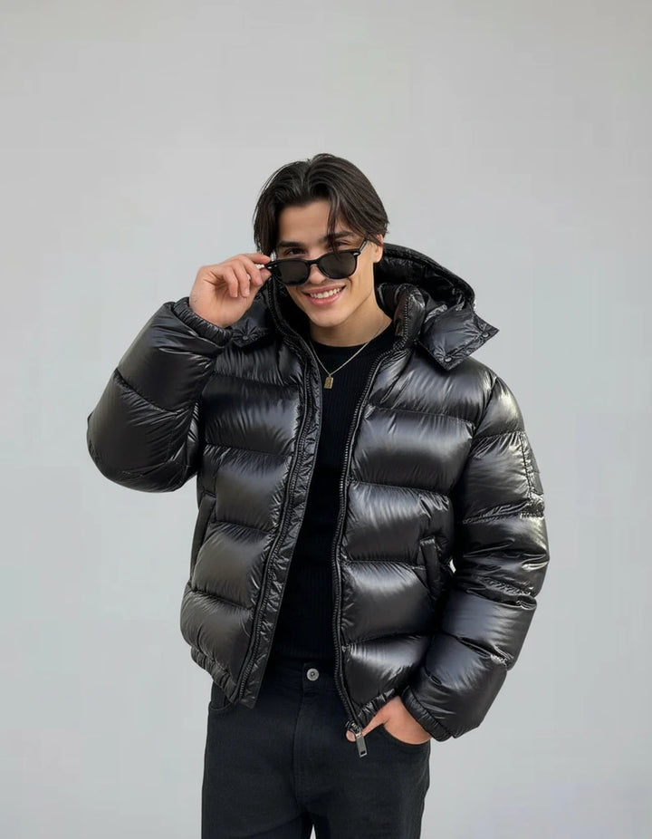 Man wearing a black puffer jacket and sunglasses against a gray background
